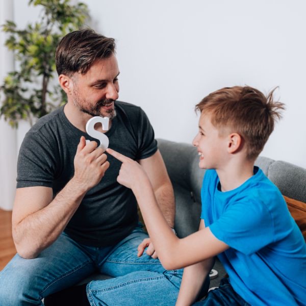 A father and his son practising the letter S together on the sofa