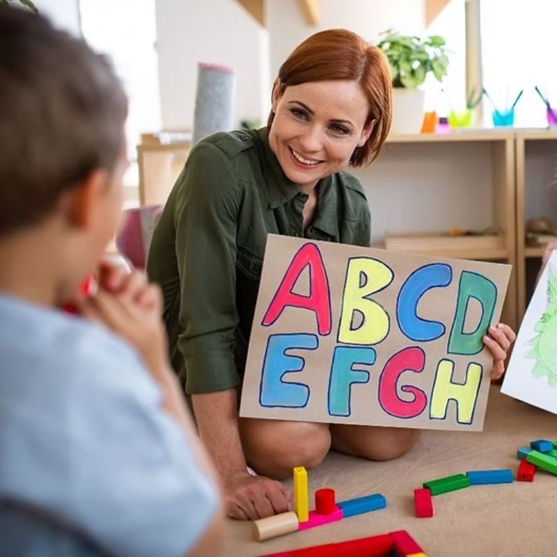 A therapist holding up a hand-drawn alphabet card for a young boy